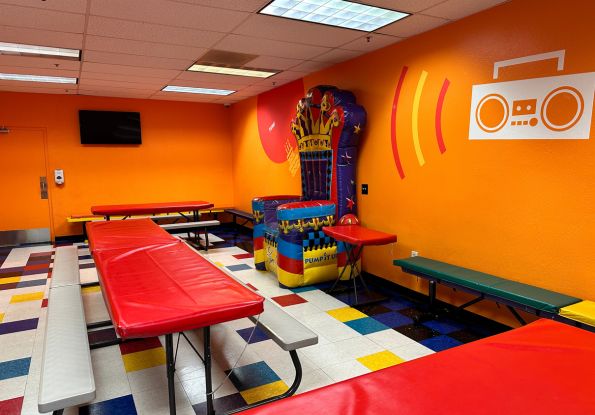Pump It Up Union City CA kids birthday party place party room with orange walls, picnic tables and inflatable birthday throne.